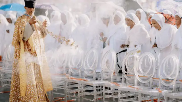 ታዳሚውን በእጣን የሚያጥኑ ቄስ እና ሴቶች 