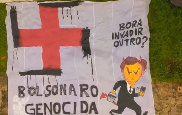 Faixa de protesto onde se lê "Bolsonaro genocida", com o desenho de um Bolsonaro com chifres e rabo de diabo e um bigodinho de Hitler, segurando um balde de tinta e um pincel, com o qual ele teria transformado a cruz vermelha símbolo dos serviços de emergência em saúde numa suástica. A faixa foi estendida em frente ao Palácio do Planalto num protesto durante a pandemia