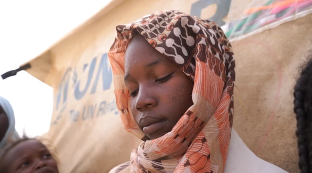 تُظهر الصورة صفاء، الفتاة السودانية البالغة من العمر 14 عاماً، وهي تجلس في مخيم للاجئين مع خمسة أطفال آخرين. 