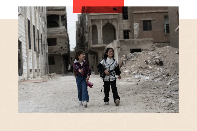 Enfants marchant et souriant, avec des gravats en arrière-plan