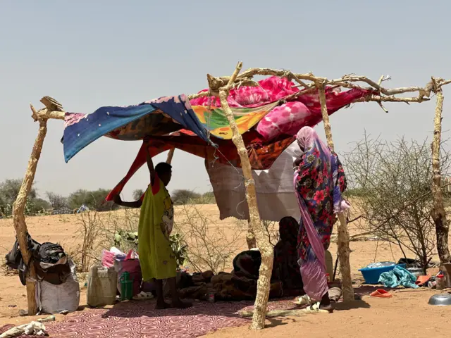 صورة تظهر نازحين سودانيين يحتمون تحت خيمة بدائية الصنع وسط منطقة شبه صحراوية.