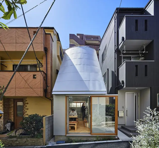 Casa estrecha de diseño contemporáneo entre edificios urbanos, con fachada curva blanca y un gran ventanal hacia la calle.
