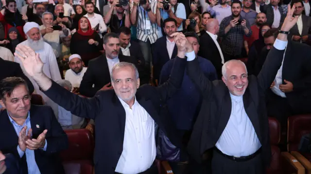 مسعود پزشکیان، نامزد ریاست جمهوری و محمدجواد ظریف، وزیر امور خارجه سابق، در یک رویداد تبلیغاتی در تهران، ایران، ۱۹ ژوئن ۲۰۲۴، علامت پیروزی را نشان می دهند