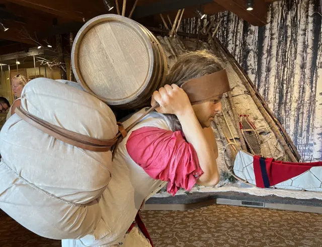 Butumbutumin ɗan asalin ƙabilar Ojibwe ɗauke da kaya a gidan adana kayan tarihi na Grand Portage