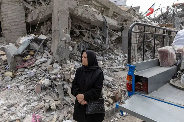 زنی در میان آوار ساختمان‌های مسکونی که چند روز پیش در پی حملات آمریکا و اسرائیل در شرق تهران ویران شده‌اند ایستاده است؛ این صحنه در ۱۲ مارس ۲۰۲۶ ثبت شده است. 