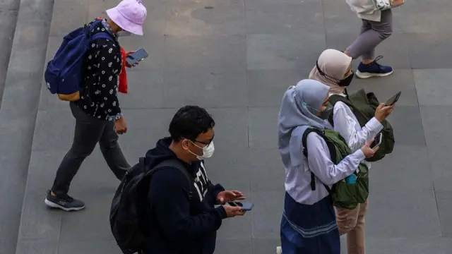 Sejumlah pekerja sedang berjalan sambil memainkan ponsel pintar mereka di Jakarta, pada 20 Juli 2022. 
