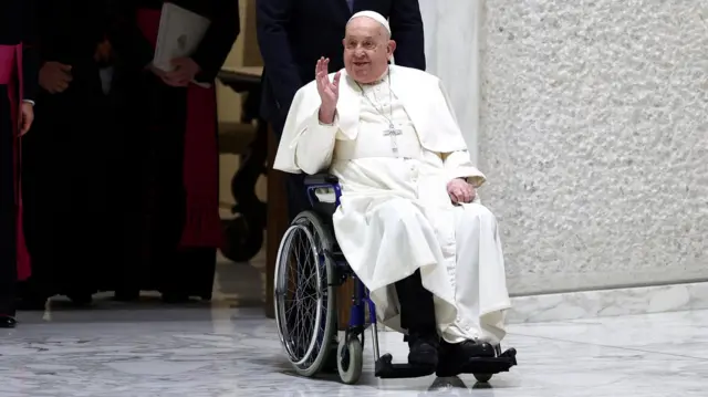 Papa Francisco acenando sentado em uma cadeira de rodas