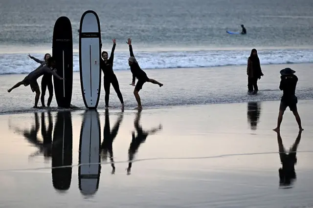 Para wisatawan berpose dengan papan selancar mereka di pantai Kuta dekat Denpasar di pulau wisata Bali, Indonesia pada 8 April 2026. (Foto oleh 