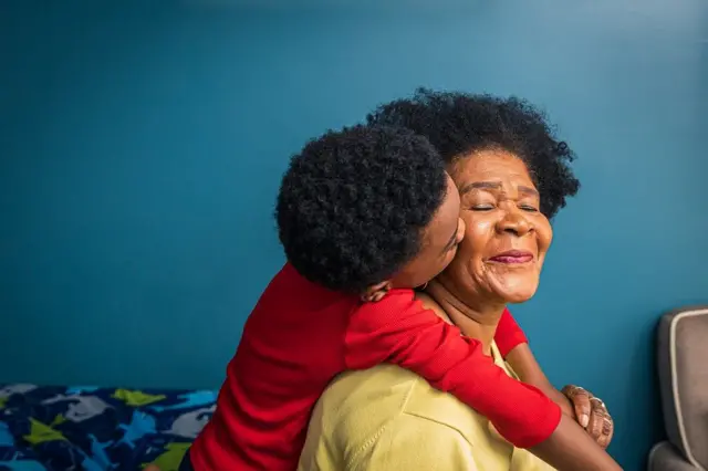 Una abuelita siendo abrazada por su nieto