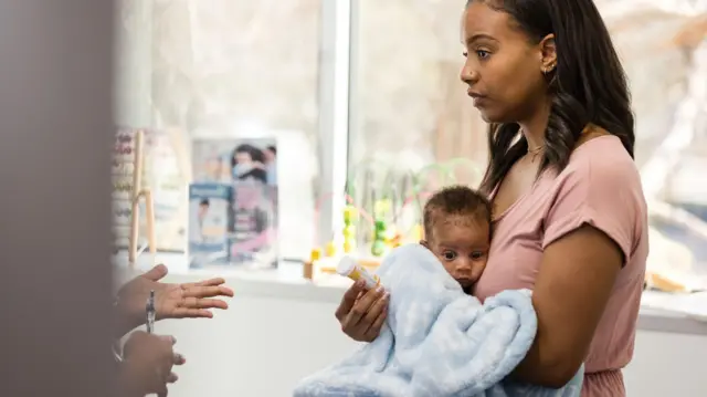 一位母亲抱着初生婴儿去看医生，看起来心不在焉、情绪低落