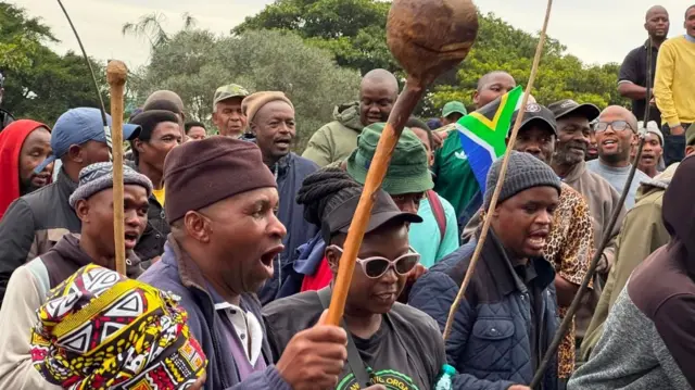 Protesters hold stick and dem dey chant