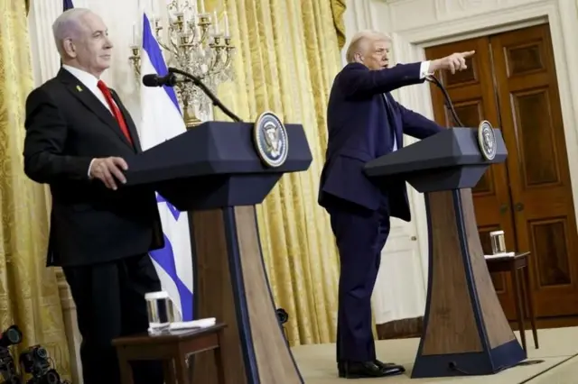 Netanyahu e Trump em frente a palanques; Trump aponta para a frente