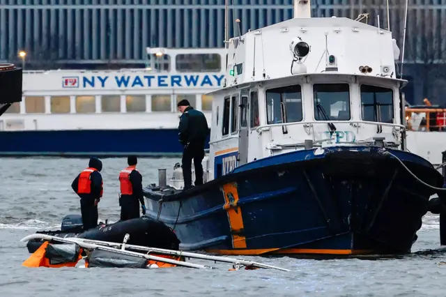 Rescue teams for di rib on di Hudson river tok with an official on a rescue boat next to di site of di crash, with di underside of di helicopter just visible above di water line and a boat for di background wey read ‘NY Waterway', for New York on 10 April