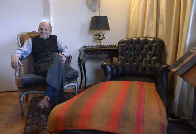 Un hombre sonriente sentado en un sillón, al lado de un diván de psicoterápia