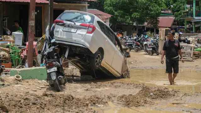 Warga melintas disamping mobil yang terseret saat banjir bandang akibat luapan Kali Lasolo di Kelurahan Sanua, Kendari, Sulawesi Tenggara, Kamis (07/03).