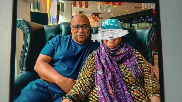 El pastelero Graham Hornigold, con una camiseta azul marino, se sienta con su madre, Dionne Marie Hanna, que lleva un baju kurung, una bufanda morada y un sombrero verde azulado, en un sofá de un restaurante.