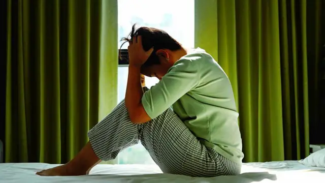 Mulher com as mãos na cabeça, sentada sobre uma cama