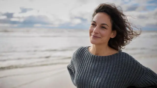 Seorang perempuan di pantai, tersenyum.