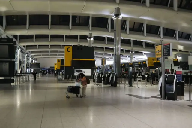 One traveler stand wit her luggage as departure boards and oda screens dey dark for Heathrow airport