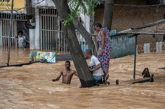 Abaturage bahagaze mu giti kugira ngo badatwarwa n'amazi y'imyuzure yari yuzuye mu muhanda, nyuma y'imvura nyinshi yaguye mu karere ka N'djili k'i Kinshasa. Ifoto yo ku itariki ya 6 Mata (4) mu mwaka wa 2025. 