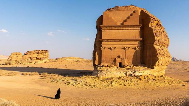 Una mujer camina junto a unas ruinas en el desierto. 