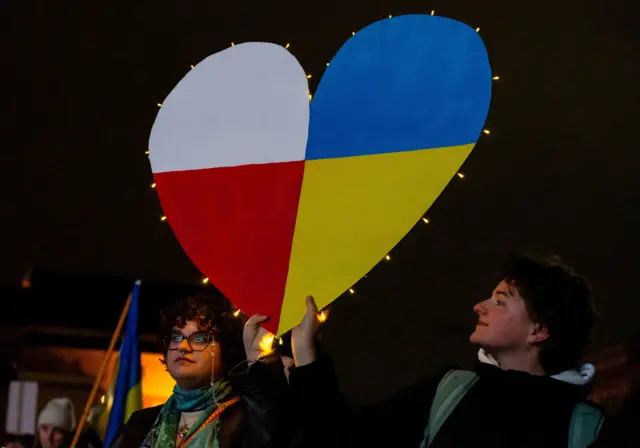 Двоє людей тримають велике картонне серце у кольорах прапорів Польщі та України