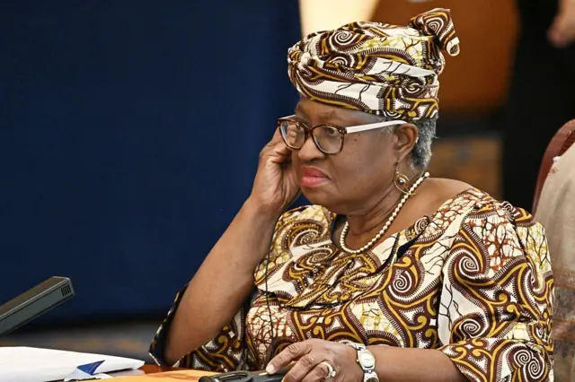 Ngozi Okonjo-Iweala en pagne à motif, elle met sa main droite sur la joue et porte des verres.
