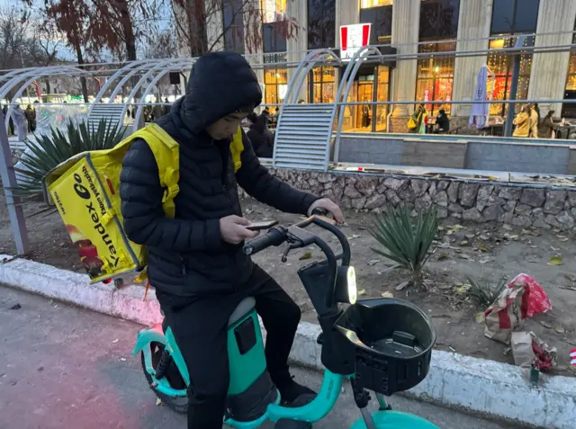 Курер Жўшқин иш устида, телефонига келган буюртмани текшираётган пайт.