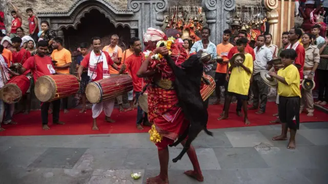 یک روحانی در جشن دیودانی، بز قربانی را بر دوش خود گرفته و می‌رقصد، معبد کاماکیا، گواهاتی در ایالت آسام هند، ۱۹ اوت ۲۰۲۲