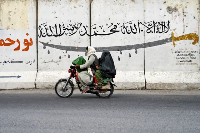 An Afghan man and a burqa-clad woman ride a motorcycle along a street on the outskirts of Kandahar on August 24, 2024