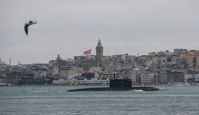 Подлодка «Ростов-на-Дону» входит в Черное море через Босфор 13 февраля 2022 года. Из воды торчит рубка плывущей субмарины, на заднем плане здания турецкого города