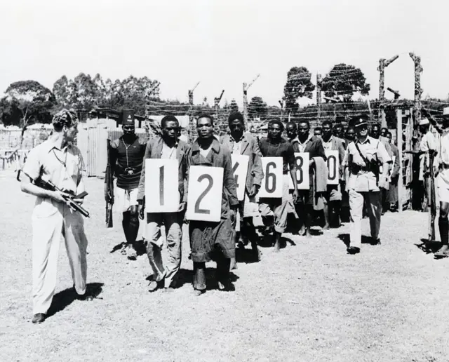 La police conduit 27 hommes accusés d’avoir participé à un récent massacre devant le tribunal de Githunguri. Ce massacre a coûté la vie à 150 Kikuyus, lorsque des terroristes Mau Mau ont attaqué le district montagneux de la réserve de Kiambu, près de Nairobi, incendiant de petits villages et brûlant vifs de nombreux habitants.