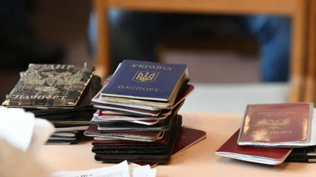 На фото три купки - крайна ліва, середня за висотою складається з паспортів "ДНР", посередині найвища - з паспортів України. Крайня права найменша - з паспортів РФ.