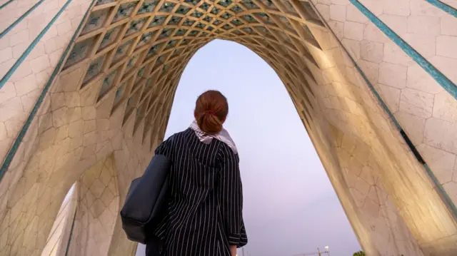 نمای پشت یک گردشگر زن که رو به برج آزادی در تهران نگاه میکند؛ نمادی از شهر و یکی از جاذبههای محبوب گردشگری.