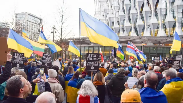 متظاهرون يحملون أعلاماً أوكرانية ولافتات مناهضة لترامب خلال المظاهرة. تجمعت الحشود خارج السفارة الأمريكية احتجاجاً على ترامب وبوتين بعد تغيير موقف ترامب تجاه أوكرانيا