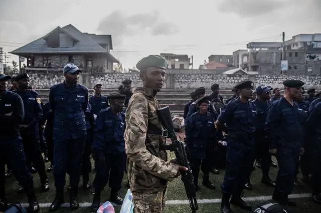 Un membre du mouvement M23 monte la garde tandis que des policiers congolais, arrivés de Bukavu, font la queue pour enrôler des civils, des policiers et d'anciens membres des Forces armées de la République démocratique du Congo (FARDC) qui auraient décidé de rejoindre volontairement le M23 à Goma, le 23 février 2025.