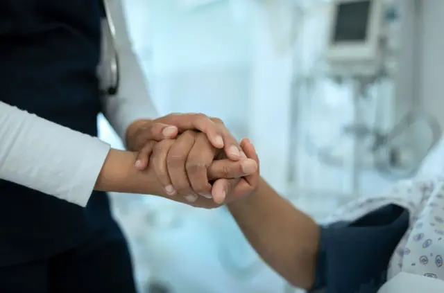 একজন রোগীর হাত দুই হাতে ধরে সান্ত্বনা দিচ্ছেন একজন চিকিৎসক