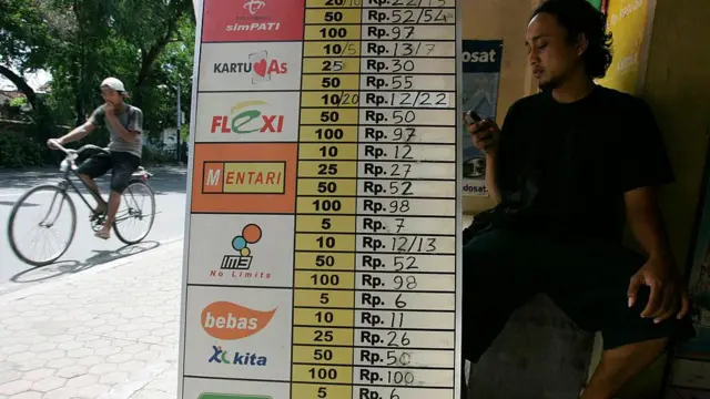 Seorang pria menggunakan telepon pintarnya saat menunggu berbelanja di toko yang menjual kuota internet di Bali, pada 6 Mei 2007.