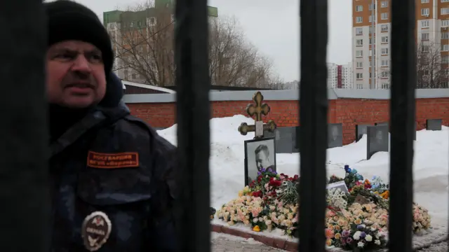 Охранник в форме, за ним — могила Навального