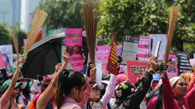 Massa aksi dari Aliansi Perempuan Indonesia membentangkan poster dan membawa sapu lidi saat aksi damai di depan kompleks DPR, Jakarta, Rabu (3/9)