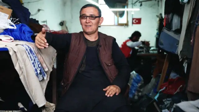 Islam Qaracha sits in a room surrounded by textiles