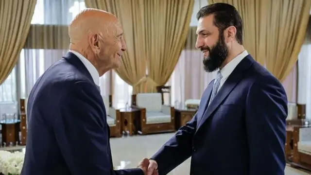 تام باراک در حال دست دادن با احمد شرع