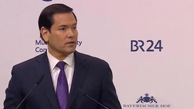 Minisitiri w'ububanyi n'amahanga w'Amerika Marco Rubio arimo kuvuga ijambo avugira mu ndangururamajwi ebyiri. Yambaye ikositimu yijimye na karuvati y'iroza n'ishati ijya kuba umweru. Ifoto yo ku wa gatandatu, ku itariki ya 14 Gashyantare (2) mu 2026, i Munich mu Budage. 