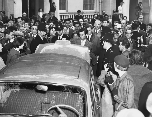 Un hombre abre el baúl de un automóvil, mientras está rodeado por varios policías londinenses y una gran cantidad de periodistas y curiososos tomando fotografías.