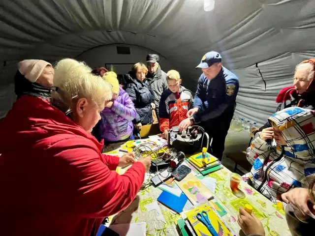 Чернігів. Люди стоять довкола зарядного пристрою у наметі пункту незламності 