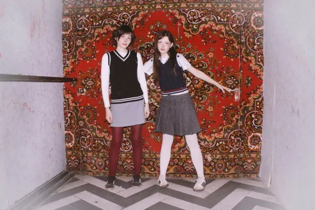 Две молодые девушки на фоне красного ковра на стене