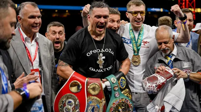 Олександр Усик з поясами WBA, WBC, WBO та IBF у важкій вазі та оточений своєю тренерською командою