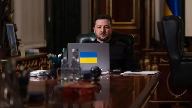 Володимир Зеленський перед ноутбуком на довгому столі темного дерева