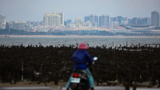 台湾金门一位女士在蚝田前停下摩托车眺望对岸中国大陆的福建厦门市区(10/3/2026)