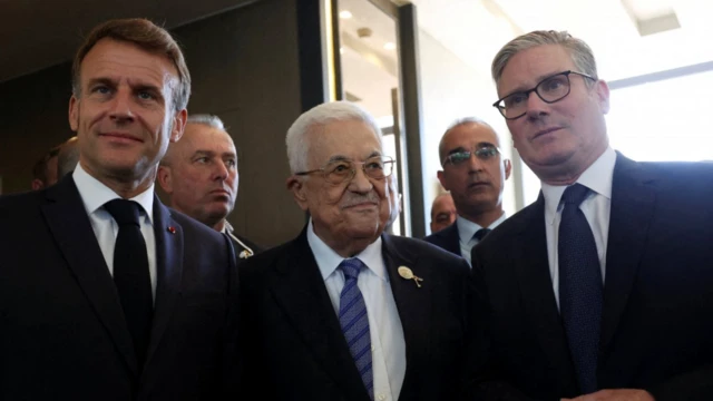 Üç erkek yan yana poz veriyor, arkalarında başka yetkililer de var